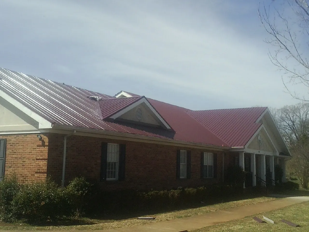 Red metal roof with gabled entries on a long brick building, from a Hail Damage Roof Repair job in Alberta