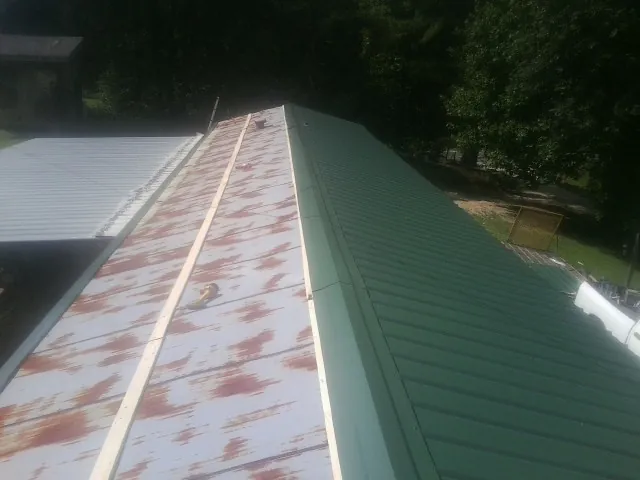 Old rusted panels beside newly installed green metal roofing — Wind Damage Roof Repair by Roofing Brothers in Alberta
