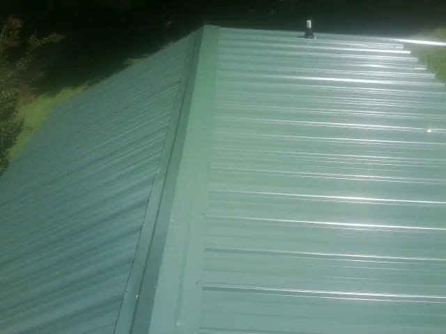 New green metal panels meeting at the ridge of a roof — Flat Roof Repair work by our crew in Alberta