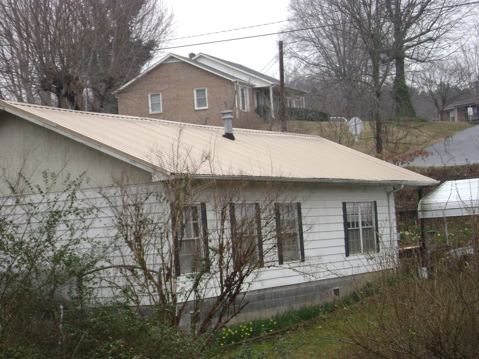 Tan metal roof on a white sided house set into a hillside — Commercial Roofing by Roofing Brothers in Alberta